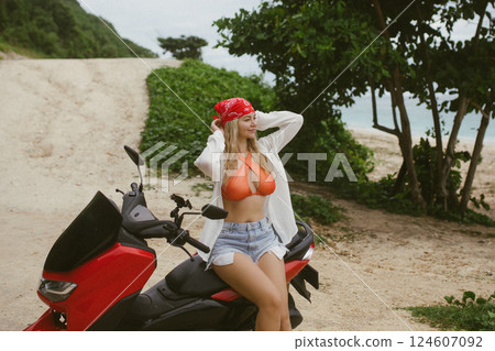 Attractive caucasian woman in a bikini swimsuit and on a bike scooter near the beach in sunny weather. Attractive caucasian woman in a bikini swimsuit and on a bike scooter near the beach in sunny weather. 124607092
