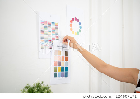 Close up of a hand sticking or taking off a printed color palette on the wall, Designer in office. 124607171