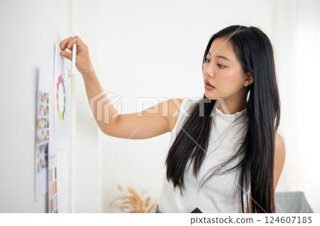 An asian woman is sticking a printed color chart or a color wheel on the wall. Designer at work. An asian woman is sticking a printed color chart or a color wheel on the wall. Designer at work. 124607185