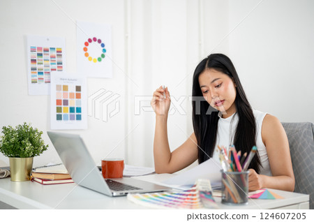 Asian woman is reading the documents while making a design on a graphic tablet and a laptop. 124607205