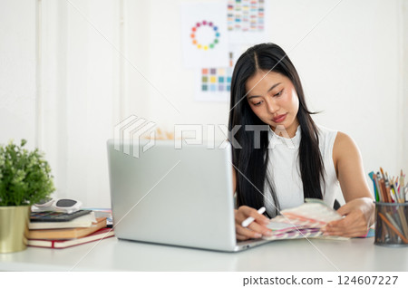 An asian woman is looking and choosing color from the printed color charts or color palette in hand 124607227