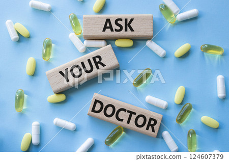 Ask Your Doctor symbol. Concept word Ask Your Doctor on wooden blocks. Beautiful blue background with pills. Medicine and Ask Your Doctor concept. Copy space 124607379