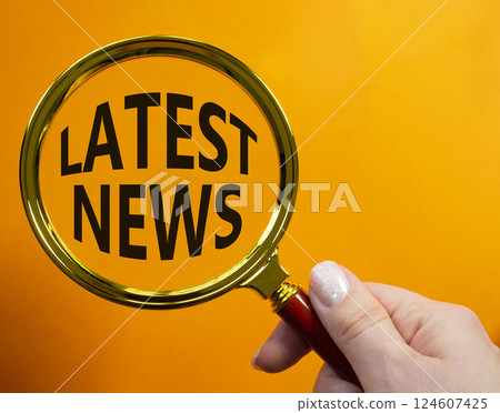 Latest News symbol. Concept word Latest News on magnifying glass. Businessman hand. Beautiful orange background. Business and Latest News concept. Copy space 124607425