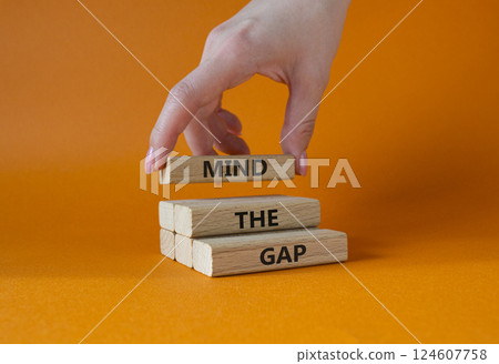 Mind the gap symbol. Concept words Mind the gap on wooden blocks. Beautiful orange background. Businessman hand. Business and Mind the gap concept. Copy space. 124607758