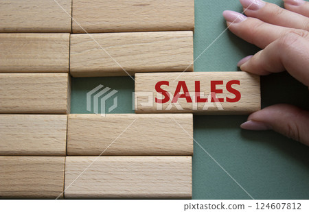 Sales symbol. Concept word Sales on wooden blocks. Businessman hand. Beautiful grey green background. Business and Sales concept. Copy space. 124607812