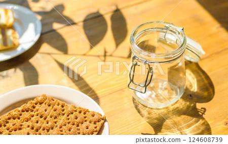 A White Plate Holds Cookie Crumbs Next to an Empty Glass Jar on a Wooden Table A White Plate Holds Cookie Crumbs Next to an Empty Glass Jar on a Wooden Table 124608739