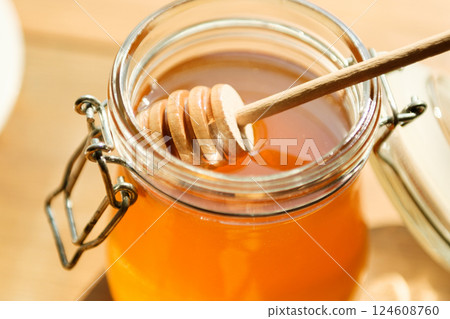 Honey Jar With Wooden Dipper, Showcasing Golden Honey in Natural Light; Perfect for Food Bloggers and Organic Markets 124608760