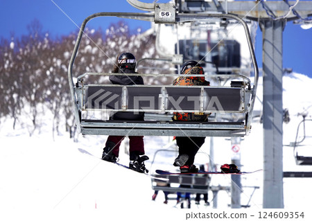Two people on the ski lift leading to the summit at a ski resort on a sunny day 124609354