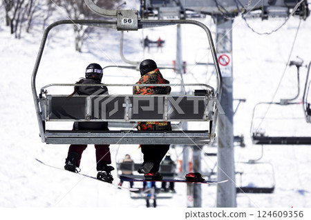 Two people on the ski lift leading to the summit at a ski resort on a sunny day Two people on the ski lift leading to the summit at a ski resort on a sunny day 124609356
