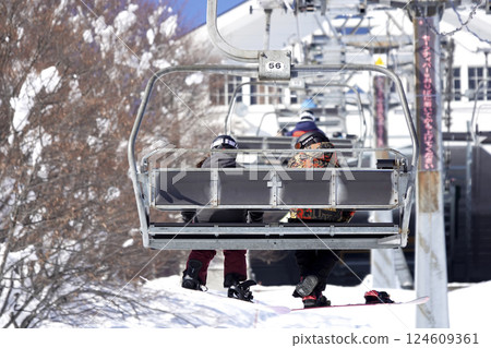 Two people on the ski lift leading to the summit at a ski resort on a sunny day 124609361