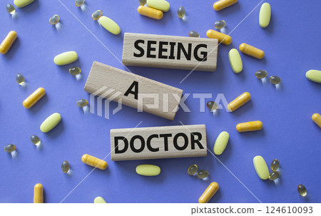 Seeing a Doctor symbol. Concept word Seeing a Doctor on wooden blocks. Beautiful purple background with pills. Medicine and Seeing a Doctor concept. Copy space Seeing a Doctor symbol. Concept word Seeing a Doctor on wooden blocks. Beautiful purple background with pills. Medicine and Seeing a Doctor concept. Copy space 124610093