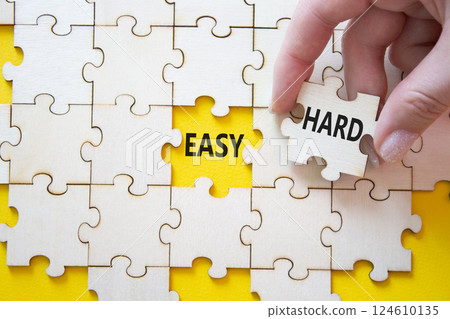 Easy or Hard symbol. Concept word Easy or Hard on wooden puzzle. Businessman hand. Beautiful yellow background. Business and Easy or Hard concept. Copy space 124610135