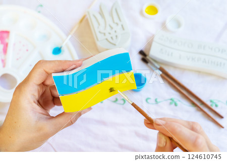 Hands painting a plaster plaque with the blue and yellow colors of the Ukrainian flag using a brush 124610745