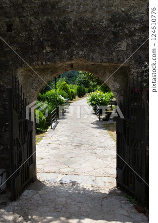 Ancient stone archway with open wrought-iron gates leads to a tranquil garden path Ancient stone archway with open wrought-iron gates leads to a tranquil garden path 124610776
