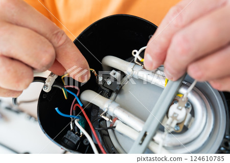 A person carefully repairs the internal wiring and components of a broken appliance A person carefully repairs the internal wiring and components of a broken appliance 124610785