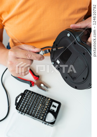A person meticulously repairs a broken appliance using a small screwdriver and a set of tools A person meticulously repairs a broken appliance using a small screwdriver and a set of tools 124610792