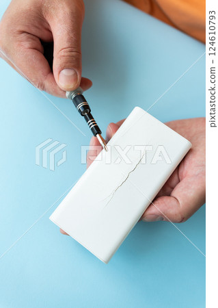 A person carefully uses a small screwdriver near a cracked white device 124610793