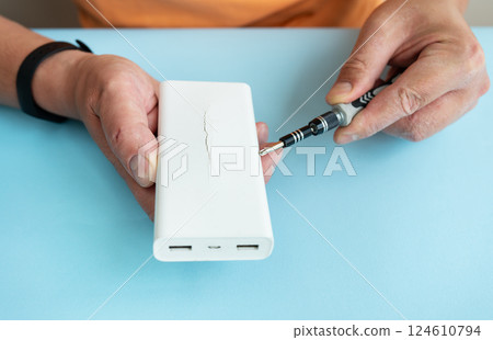 A person repairs a cracked power bank using a small screwdriver 124610794