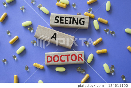 Seeing a Doctor symbol. Concept word Seeing a Doctor on wooden blocks. Beautiful purple background with pills. Medicine and Seeing a Doctor concept. Copy space 124611100