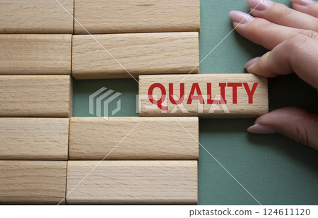 Quality symbol. Concept word Quality on wooden blocks. Businessman hand. Beautiful grey green background. Business and Quality concept. Copy space. Quality symbol. Concept word Quality on wooden blocks. Businessman hand. Beautiful grey green background. Business and Quality concept. Copy space. 124611120