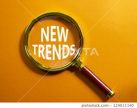 New Trends symbol. Magnifying glass with words New Trends. Beautiful orange background. Business and New Trends concept. Copy space. 124611140