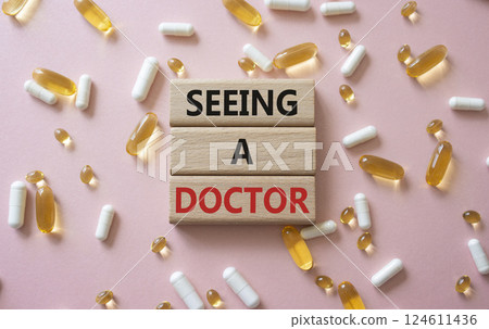 Seeing a Doctor symbol. Concept word Seeing a Doctor on wooden blocks. Beautiful pink background with pills. Medicine and Seeing a Doctor concept. Copy space Seeing a Doctor symbol. Concept word Seeing a Doctor on wooden blocks. Beautiful pink background with pills. Medicine and Seeing a Doctor concept. Copy space 124611436