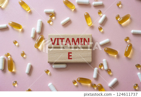 Vitamin E symbol. Concept word Vitamin E on wooden blocks. Beautiful pink background with pills. Medicine and Vitamin E concept. Copy space Vitamin E symbol. Concept word Vitamin E on wooden blocks. Beautiful pink background with pills. Medicine and Vitamin E concept. Copy space 124611737