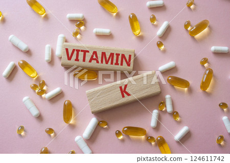Vitamin K symbol. Concept word Vitamin K on wooden blocks. Beautiful pink background with pills. Medicine and Vitamin K concept. Copy space Vitamin K symbol. Concept word Vitamin K on wooden blocks. Beautiful pink background with pills. Medicine and Vitamin K concept. Copy space 124611742