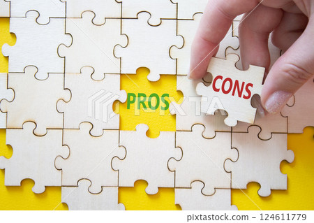Pros vs Cons symbol. Concept word Pros vs Cons on wooden puzzle. Businessman hand. Beautiful yellow background. Business and Pros vs Cons concept. Copy space 124611779