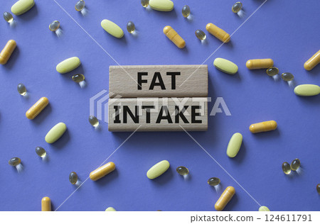 Fat Intake symbol. Concept word Fat Intake on wooden blocks. Beautiful purple background with pills. Medicine and Fat Intake concept. Copy space 124611791