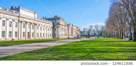 Visitors stroll along the spacious lawns of the Old Royal Naval College in Greenwich, London. The clear blue sky enhances the beauty of the historic architecture and lush greenery. 124611886