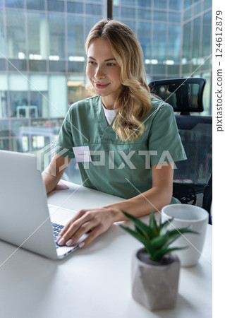Female doctor sitting at table with laptop in workplace in hospital 124612879
