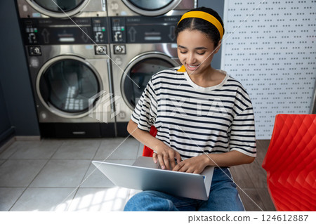 Woman in laundry shop using wireless internet on notebook while waiting for clean clothes 124612887