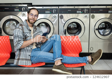 Man tapping and texting message on smartphone while sitting in public laundromat 124612907