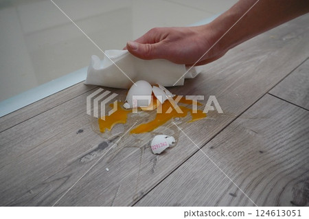 Close up the white egg fall and broken on wooden floor. crushed egg with cleaning hand 124613051