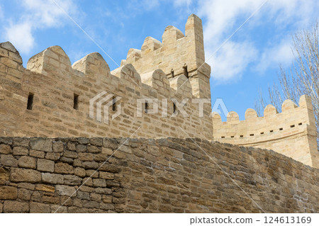 Historic stone fortification walls are under a vivid blue sky with clouds. Baku 124613169