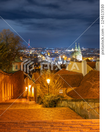 Stunning view from the Prague Castle Staircase reveals the city skyline at night. Street lamps light the cobblestone path, highlighting the historic architecture and distant spires. 124613580