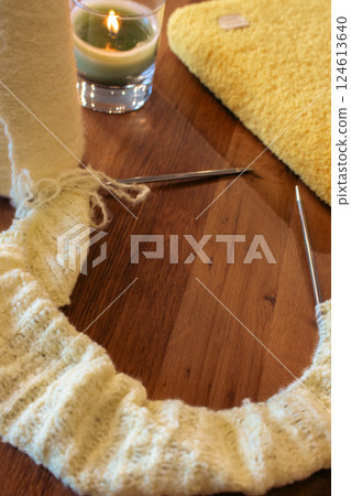 Yellow knitting pattern with knitting needles and glowing candle. Knitted fashion. Cotton knitting crochet with knitting needles and knitted bookcase. Knitting hobby. Handmade knitted clothing. 124613640