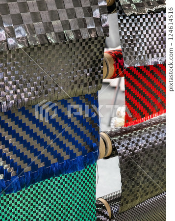 Various carbon fiber fabric samples displayed on rolls for material testing and selection in a manufacturing facility 124614516