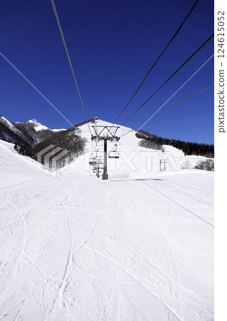 A ski resort on a clear day with a lift leading to the summit and a wide, pure white slope 124615052