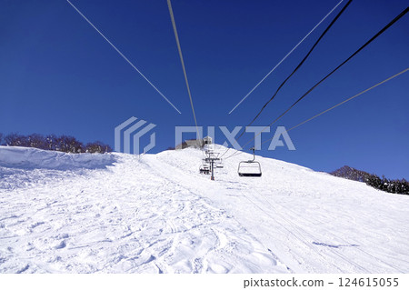 A ski resort on a clear day with a lift leading to the summit and a wide, pure white slope A ski resort on a clear day with a lift leading to the summit and a wide, pure white slope 124615055