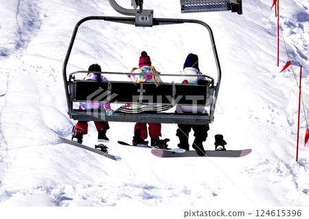 A family riding a ski lift to the top of a sunny ski resort A family riding a ski lift to the top of a sunny ski resort 124615396