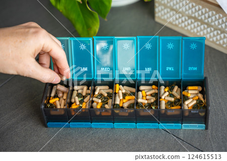 Man taking pills and supplements from his weekly pill organizer. Concept of daily medication intake and health routine Man taking pills and supplements from his weekly pill organizer. Concept of daily medication intake and health routine 124615513