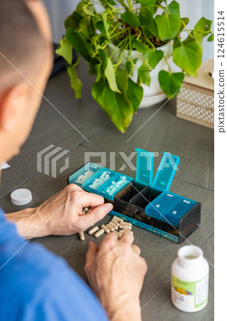 Man sorting his pills and supplements into a weekly pill organizer. Concept of medication management and daily health routine 124615514