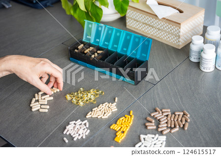 Close up view of Man hand sorting his pills and supplements into a weekly pill organizer. Concept of medication management and daily health routine 124615517