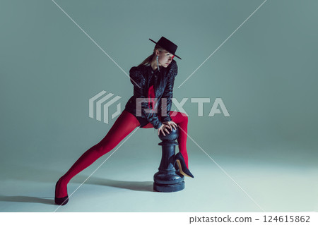 Young woman in dark avant-garde outfit controls chessboard with sharp gaze, embodying intellect and grace. 124615862