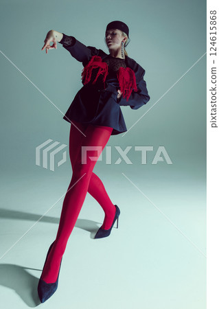 Young woman in black jacket with red fringe, red tights, and heels leaning forward, expressive hand movement. Young woman in black jacket with red fringe, red tights, and heels leaning forward, expressive hand movement. 124615868