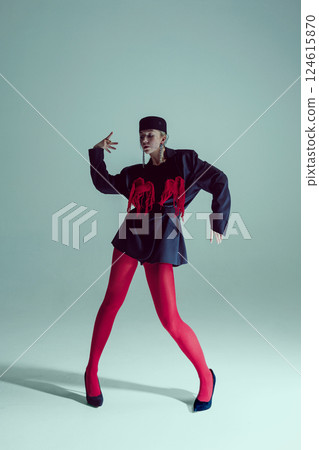 Young woman in black oversized blazer, red tights, and heels posing with angular stance, hand gesture exuding confidence. Young woman in black oversized blazer, red tights, and heels posing with angular stance, hand gesture exuding confidence. 124615870