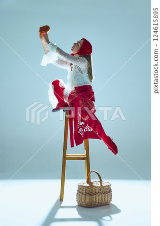 Young woman in white lace dress and red bonnet raising bread toward light, arching back in dramatic movement. Concept of surreal performance 124615895