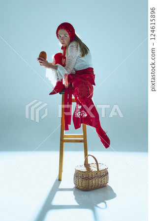 Young woman in layered white lace and red fabric crouched on stool, gripping bread, piercing gaze against white background. Young woman in layered white lace and red fabric crouched on stool, gripping bread, piercing gaze against white background. 124615896